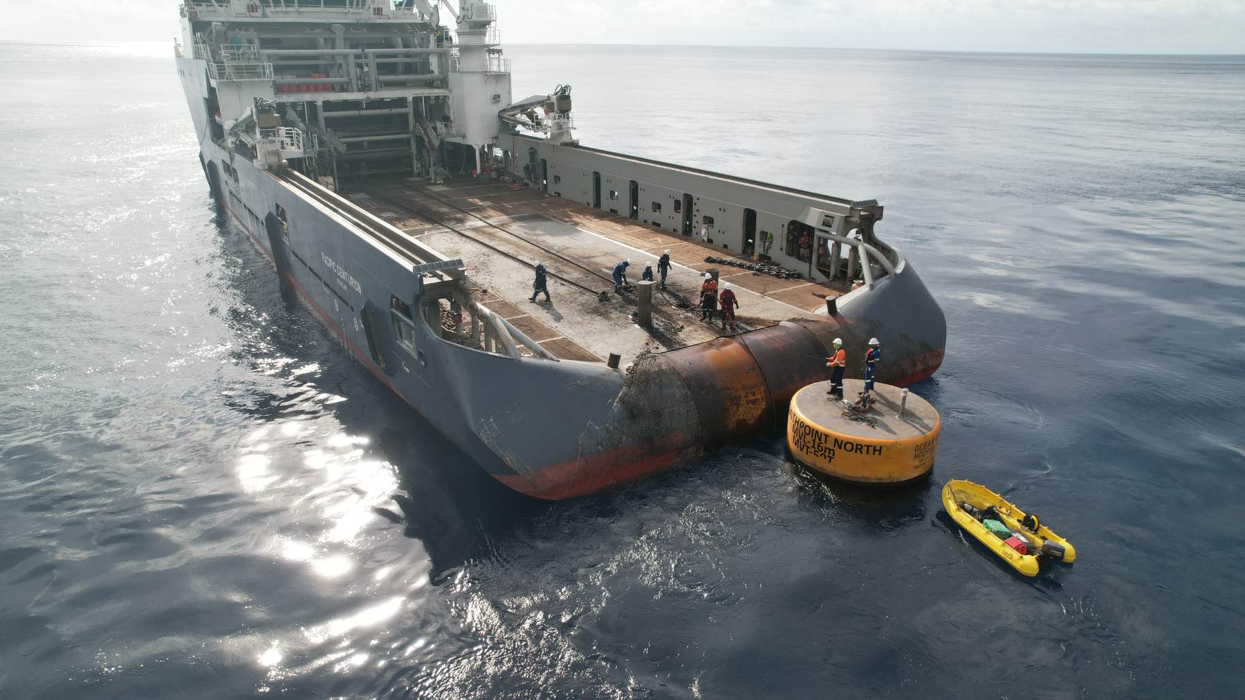 Crew working mooring gear on deck with workers standing on a buoy alongside