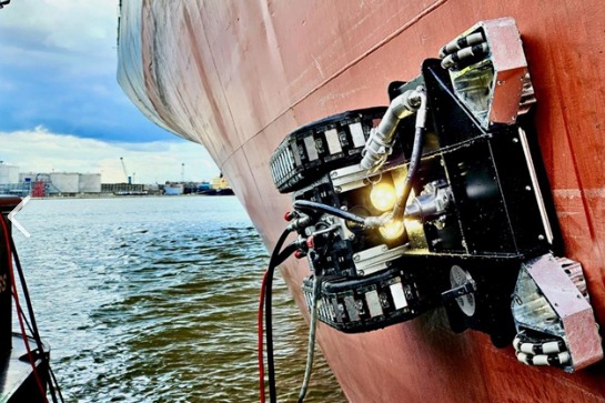 Hull crawler with lights on working the bow of a ship above the waterline