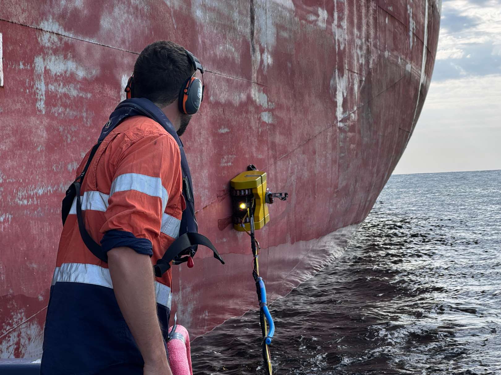 Operator supervising a hull crawler working at a ship's waterline