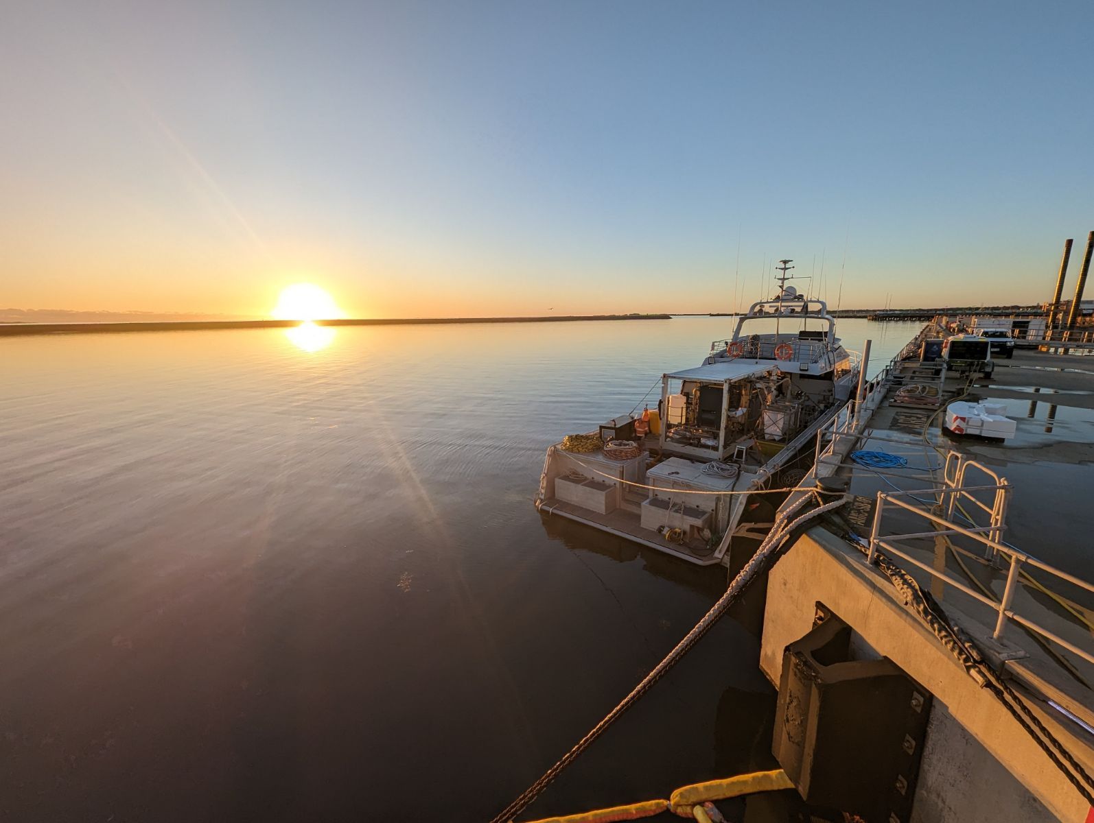 Sunrise over a calm harbour with a work vessel alongside the wharf