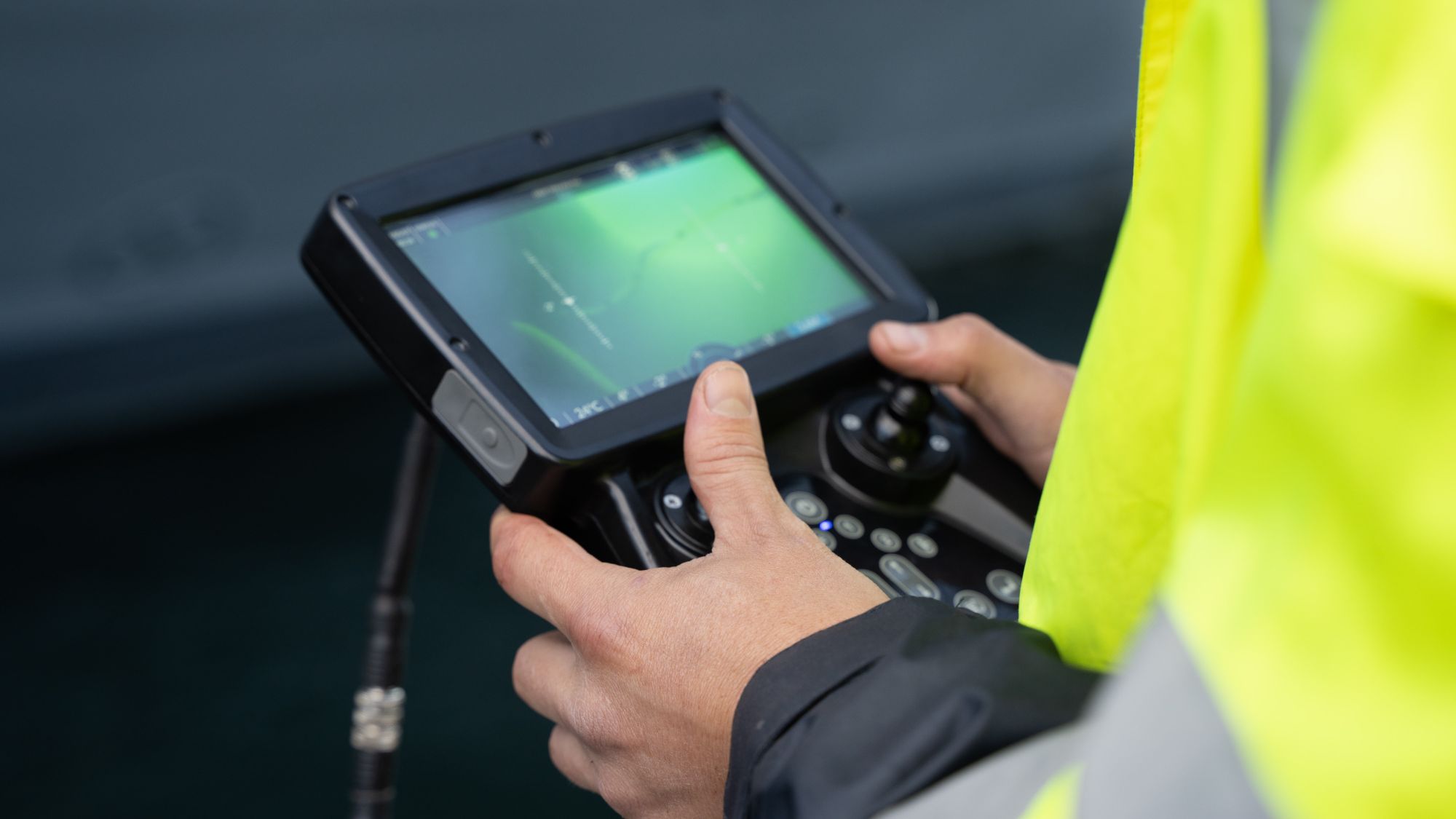 Operator's hands on an ROV controller showing a live underwater feed