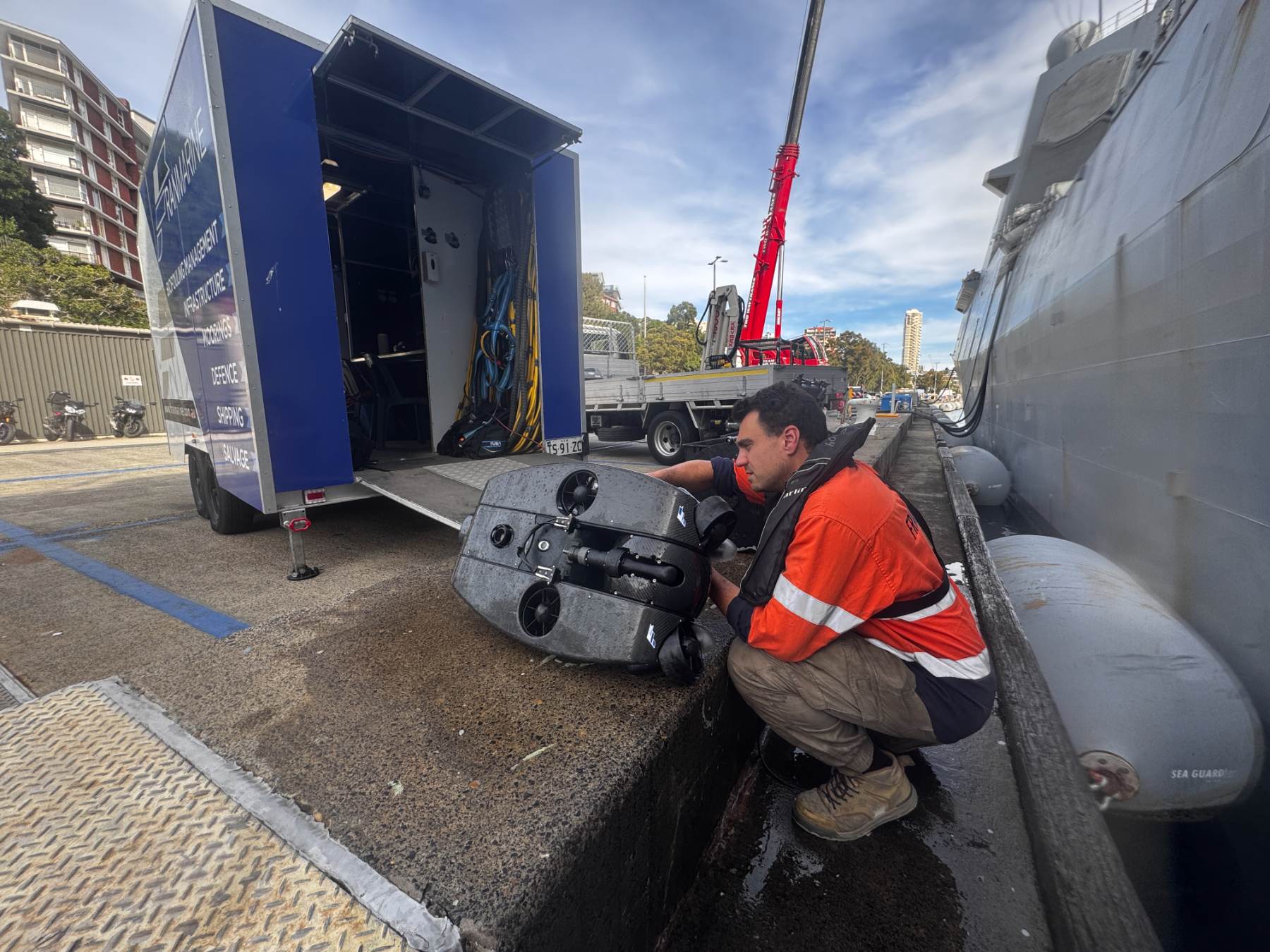 Technician preparing an ROV beside a service trailer on the wharf